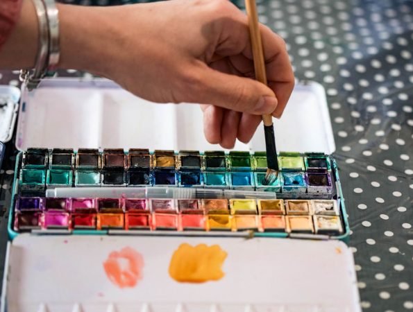 Main tenant un pinceau dans une boîte d’aquarelle pour un atelier créatif à Mons